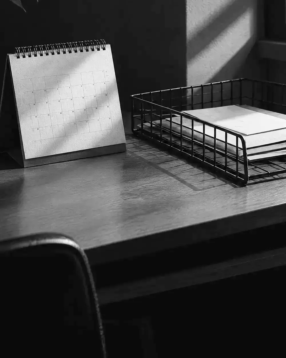 Tischkalender und Drahtkorb mit Post auf einem Holztisch im harten Seitenlicht