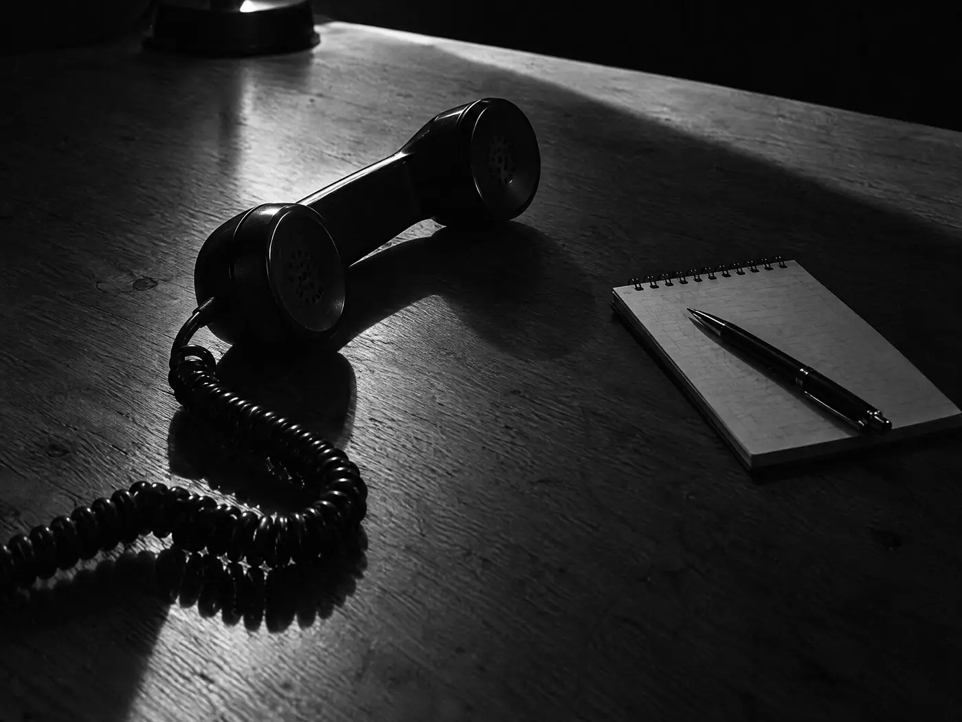 Telefonhörer mit Spiralkabel neben einem Notizblock mit Bleistift auf einem Holztisch