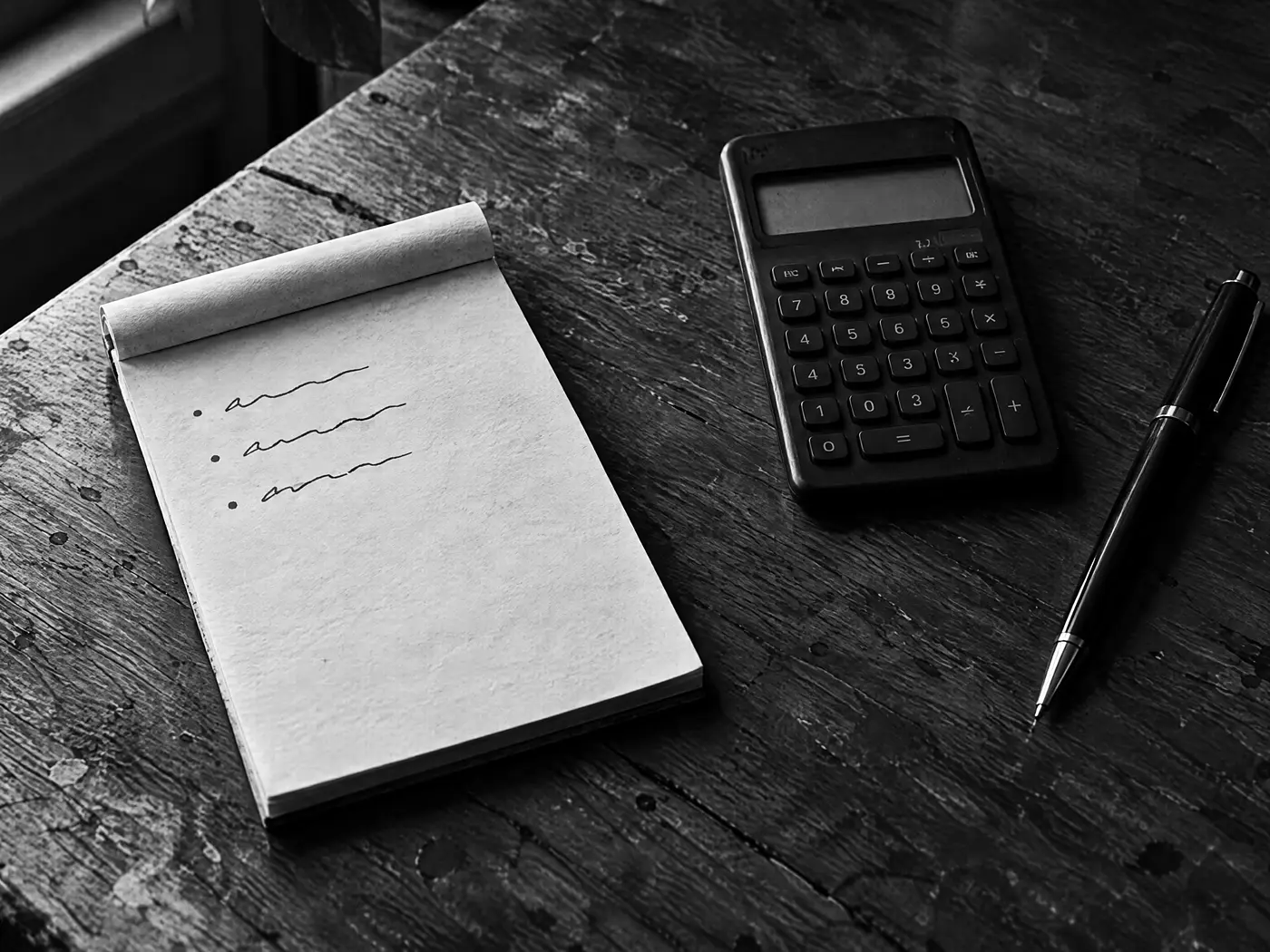 Notizblock mit handschriftlichen Zahlen, Taschenrechner mit dunklem Display und Bleistift auf einem Holztisch