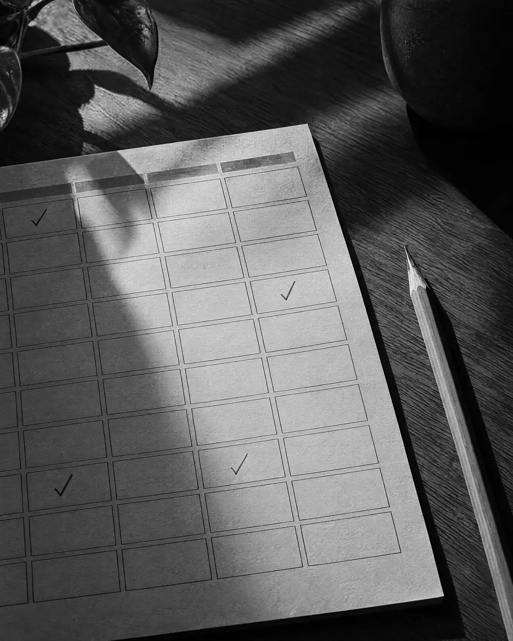 Papier-Terminplan mit angekreuzten Feldern und ein Bleistift auf einem Holztisch, hartes Licht