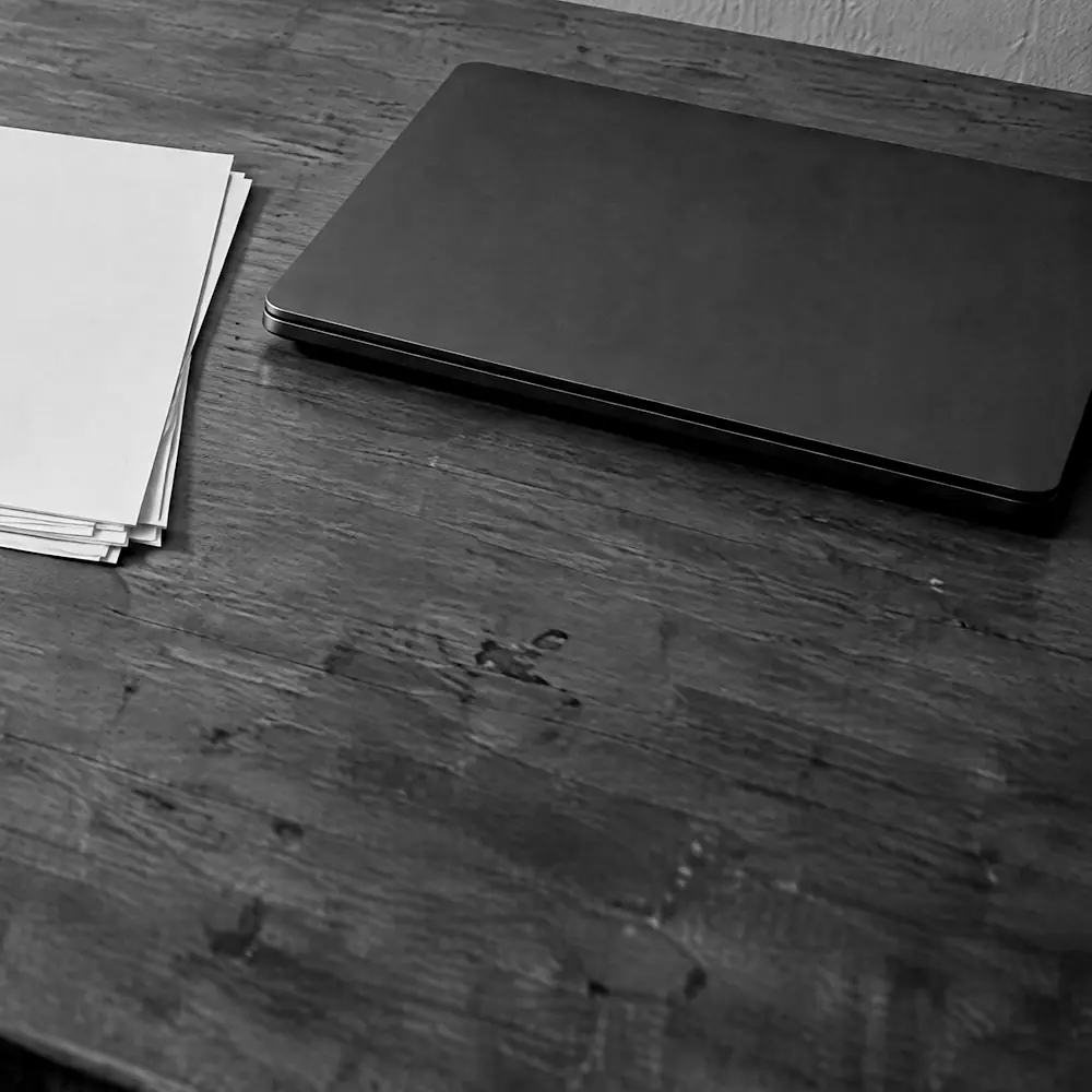 Stapel Papier und geschlossener Laptop auf einem dunklen Holztisch