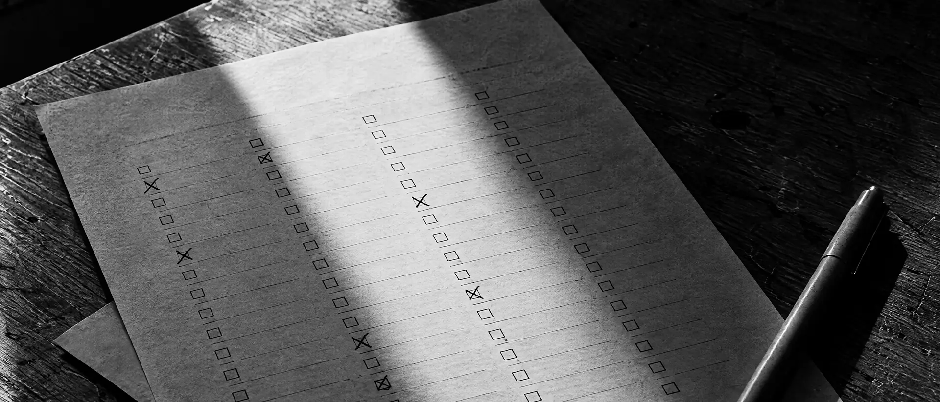 Formularblatt mit Reihen kleiner Kästchen, einzelne mit Bleistift durchgestrichen, daneben ein Stift auf einem Holztisch