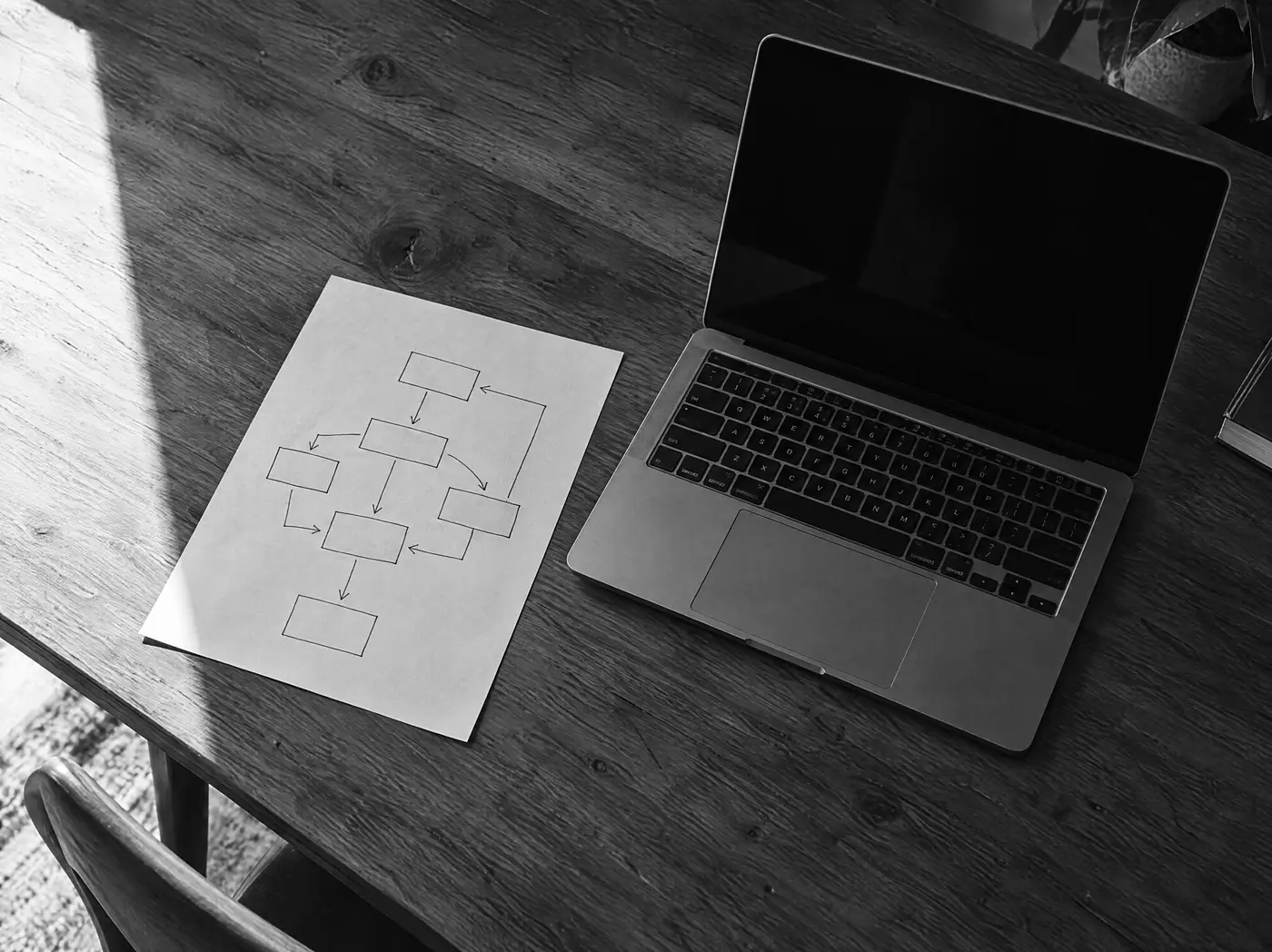 Handgezeichnete Datenfluss-Übersicht mit Kästchen und Pfeilen auf einem Holztisch, daneben ein aufgeschlagener Laptop mit dunklem Bildschirm